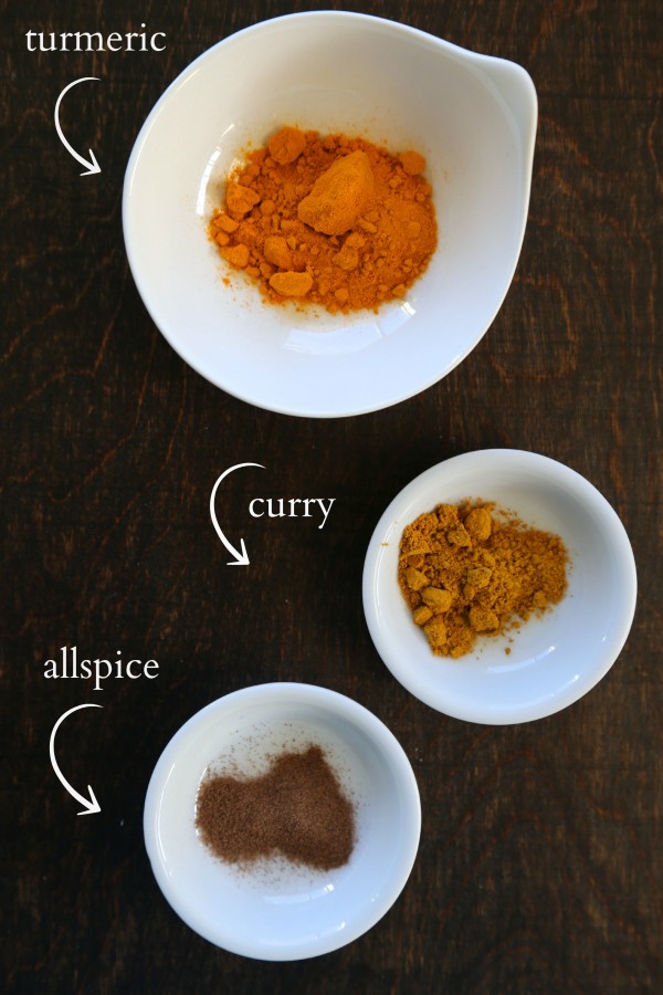 Three small bowls with filled with turmeric, allspice, and curry. 