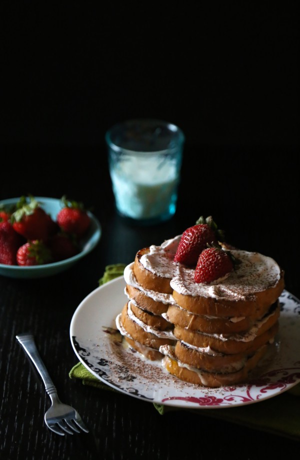 Stack of tres leches french toast with cinnamon whipped cream and strawberries. 