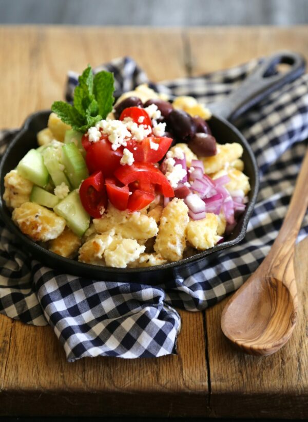 Greek gnocchi skillet topped with cucumbers, tomatoes, olives, onions, and feta.