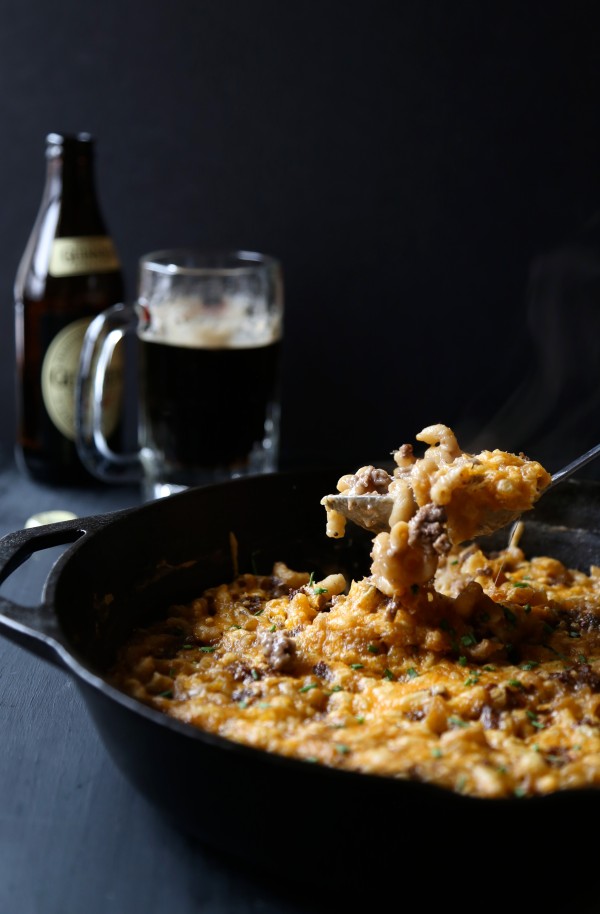 Spoon digging into skillet with Guinness mac and cheese and beef.