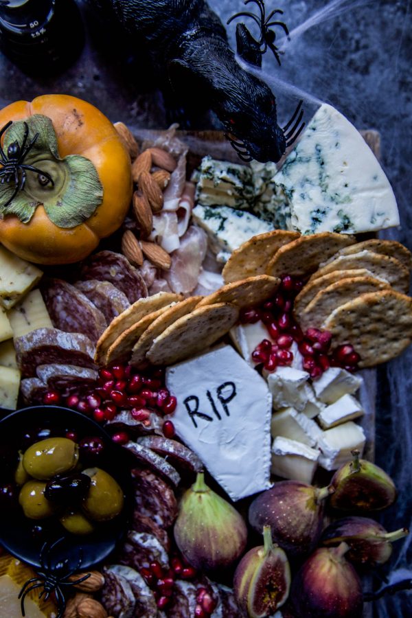 Close up of Halloween charcuterie board showing a gourd, meats, cheeses, crackers and pomegranate seeds.
