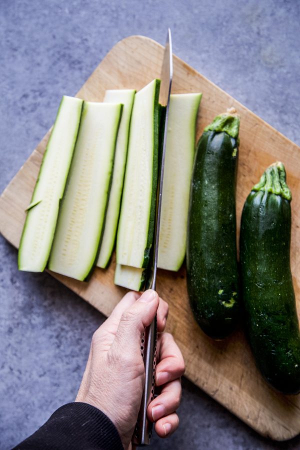 zucchini being sliced on a cutting board