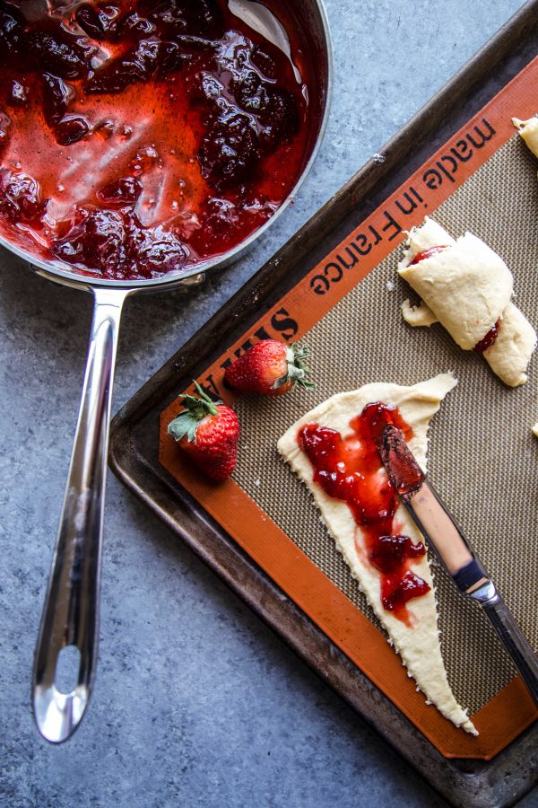 strawberry jam being spread onto a croissant dough