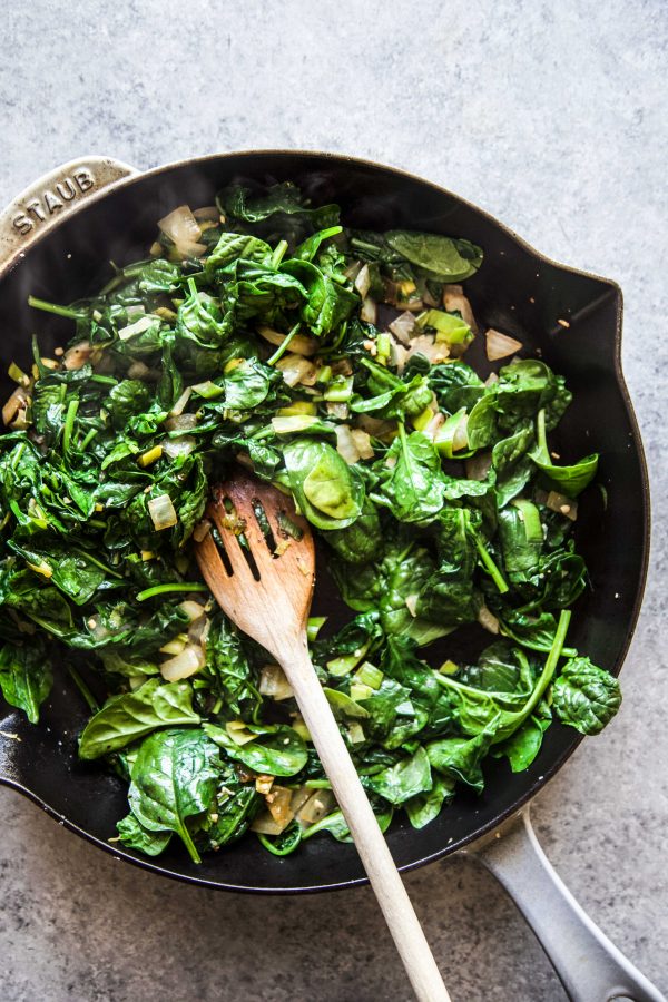 spinach cooking in a skillet with other veggies