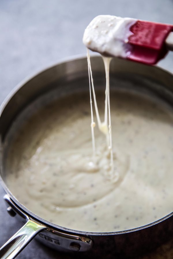 Cheese sauce in a skillet and a spatula dripping with cheese.