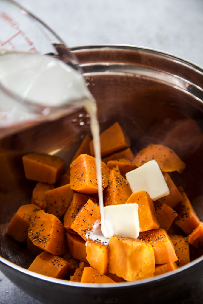 cream being poured into a bowl filled with sweet potatoes